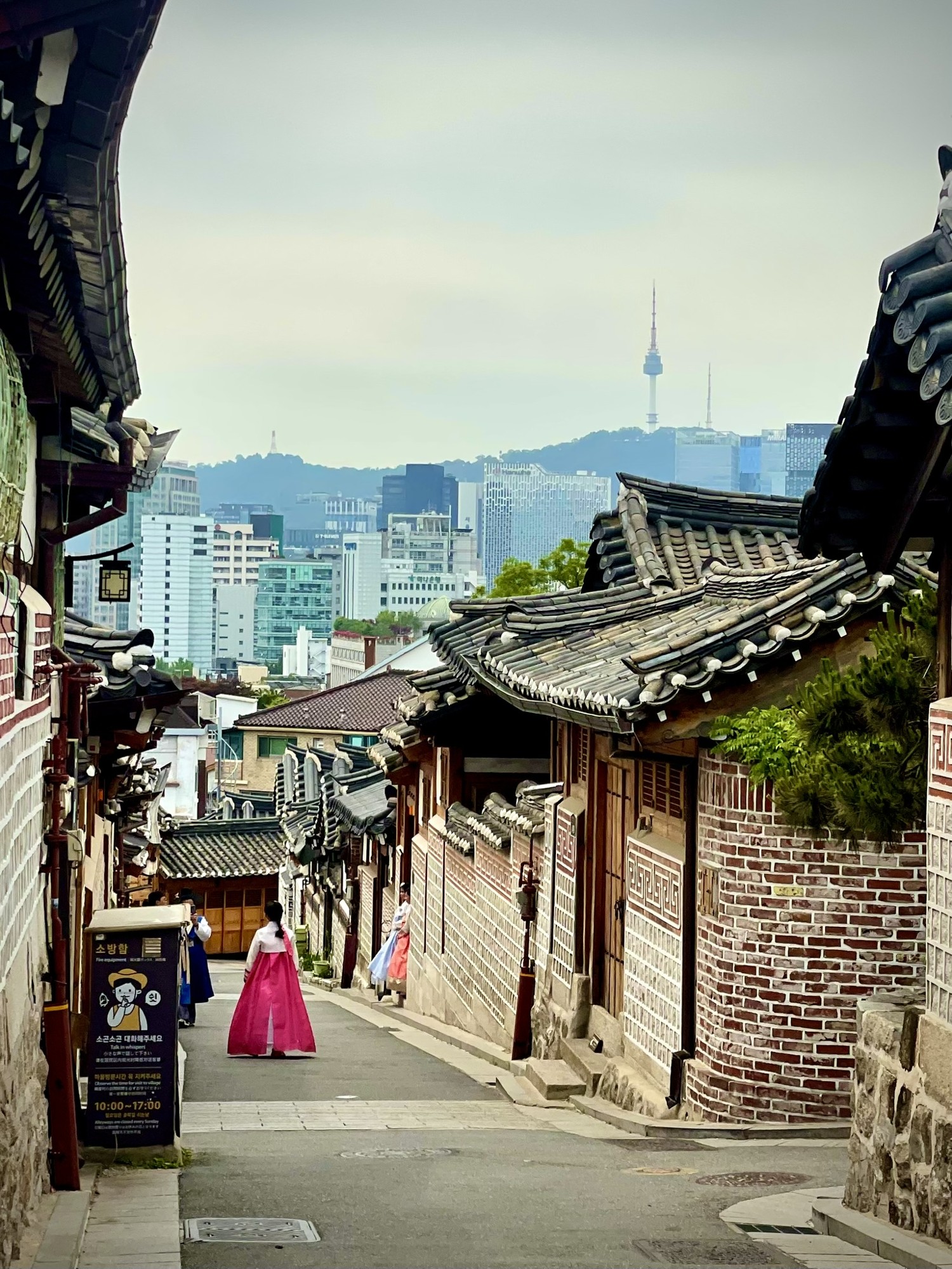 A sloping street of traditional buildings with a city skyline beyond