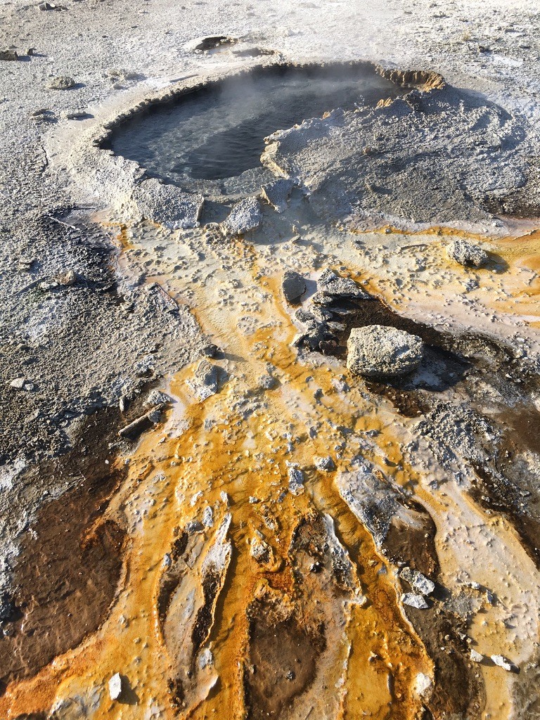 A dark geothermal pool surrounded by mineral deposits